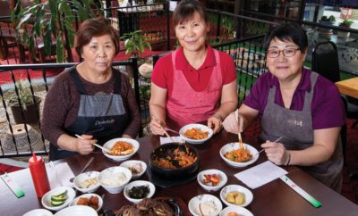 Hyun Bun Shin, Sun Hee Lockhart and Hae Lee sit at a table with several dishes at the Sisters Korean Restaurant