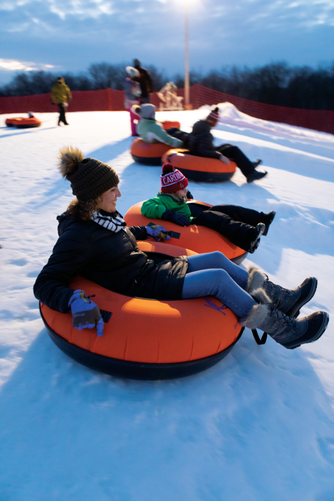 Adults and kids slide down the hill at Koteewi Run Seasonal Slopes
