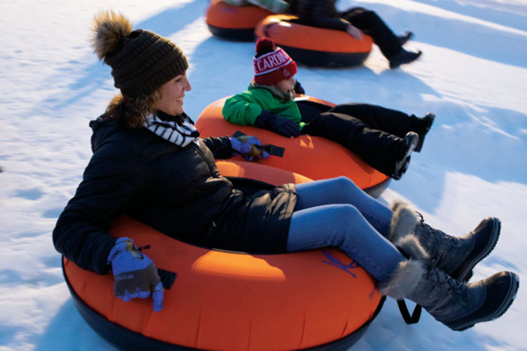 Adults and kids slide down the hill at Koteewi Run Seasonal Slopes