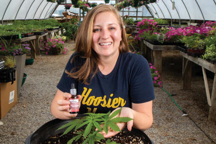 Kelly Linne sits with a young hemp plant and CBD oil products
