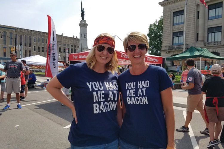 Two women in matching "You had me at bacon" shirts