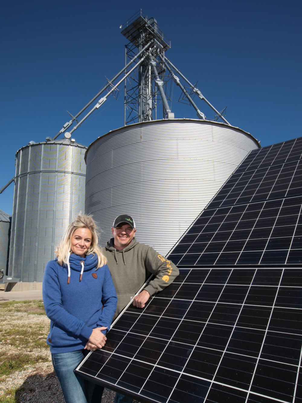 Kelli and Ryan Chalfant with the solar panels and the grain bins in the background