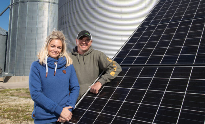 Kelli and Ryan Chalfant with the solar panels and the grain bins in the background