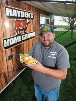 Bobby Hayden holding a cheeseburger standing next to the Hayden's Home Grown Food Truck