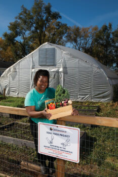 Danielle Guerin holds a box of produce standing by a Soul Food Project sign