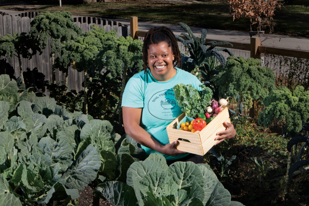 Danielle Guerin holds a box of produce standing in a field with a variety of greens growing