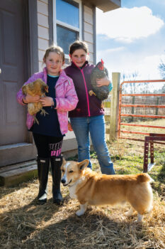 Hannah and Kate holding chickens with one of the family's dogs