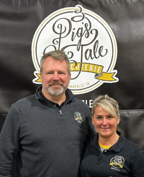 Troy and Wendee in front of Pig's Tale Charcuterie sign 