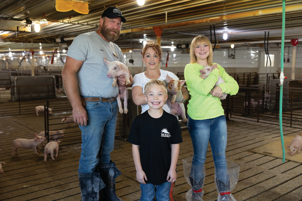 Brian Homan, Jessica, John and Isabelle holding piglets inside the pig barn