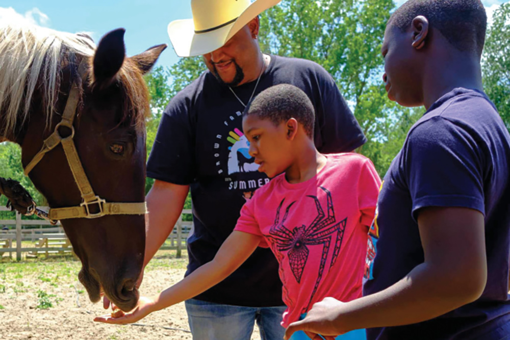 Chris Brown shows two two young boys how to feed horse