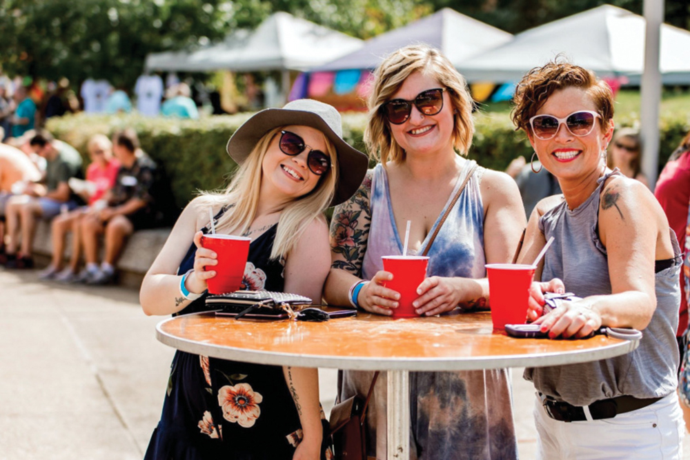 Three women pose for a photo holding drinks at the Evansville Taco Festival